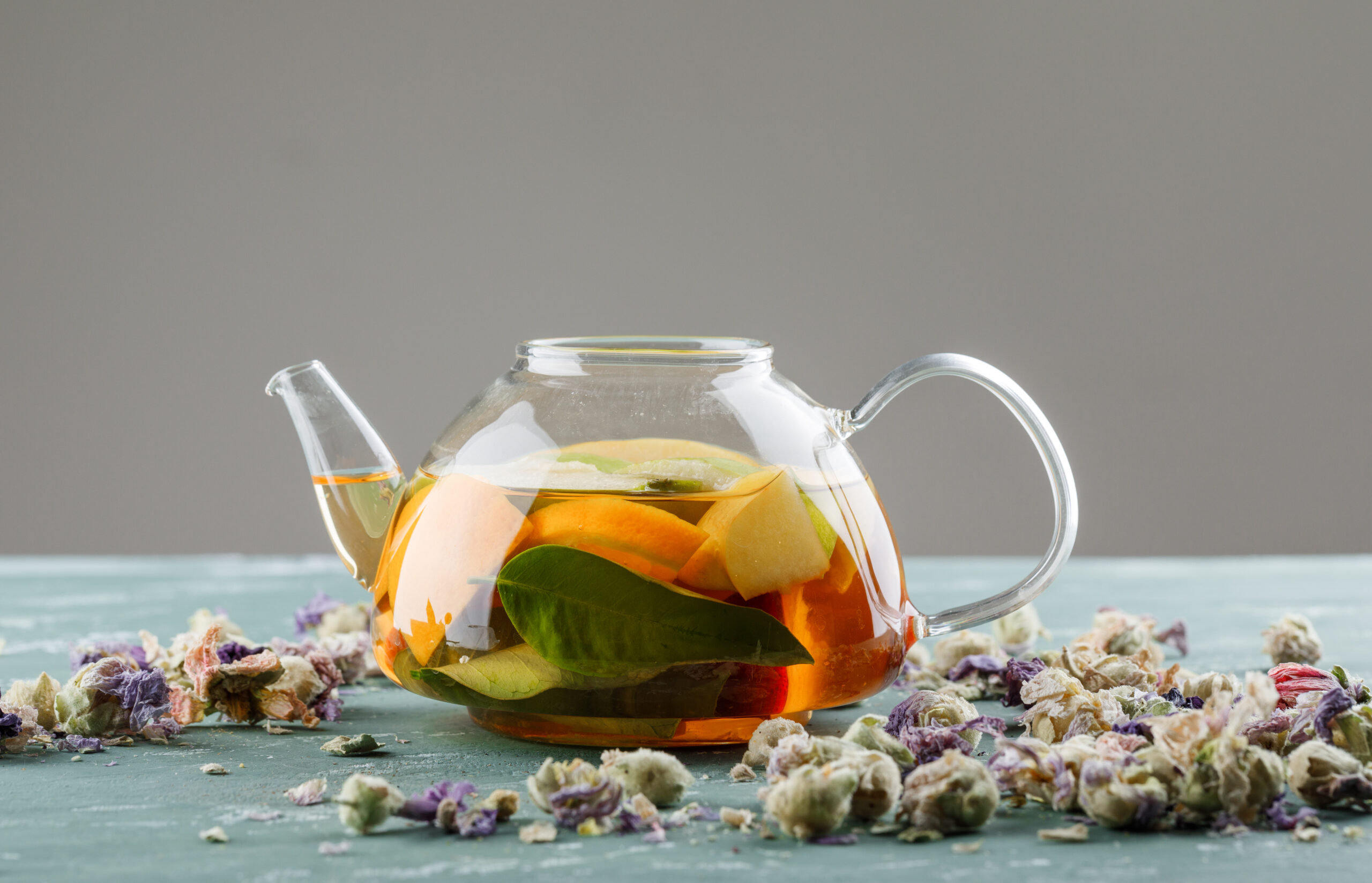 Fruit infused water in a teapot with dried flowers side view on plaster and grey background
